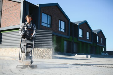 Male Worker using vibratory plate compactor to firm soil at worksite. builder. After laying of...