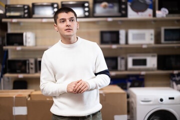 Guy customer inspect product range and selects electric iron. Client in hardware store picks up household appliances. Store of household appliances and household goods, showroom