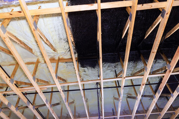 Home renovation process showing ceiling beams painted black over insulated surface.