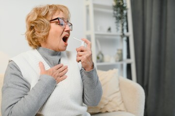 A woman is comfortably settled on her couch, using a soothing throat spray while surrounded by an...