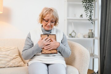 Photo of attractive aged woman look photo frame nostalgia remember sit couch home