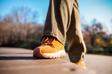 Close view of brown sneakers walking on dirt path with fallen leaves, autumn outdoor activity and...