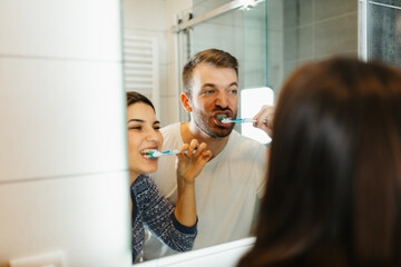 Young happy couple brushing teeth together in a modern bathroom. Morning routine and dental hygiene concept