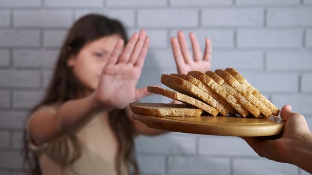 Girl refusing bread. Unhappy young girl with celiac disease refusing to eat bread with a stop gesture, demonstrating a gluten-free diet and highlighting the challenges of food allergies