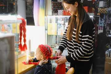 Hairstylist creating red braided hairstyle using synthetic hair extensions on child at beauty store, demonstrating hair braiding technique