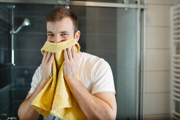 Man drying his face with a soft white towel in a modern bathroom. Morning grooming and hygiene routine
