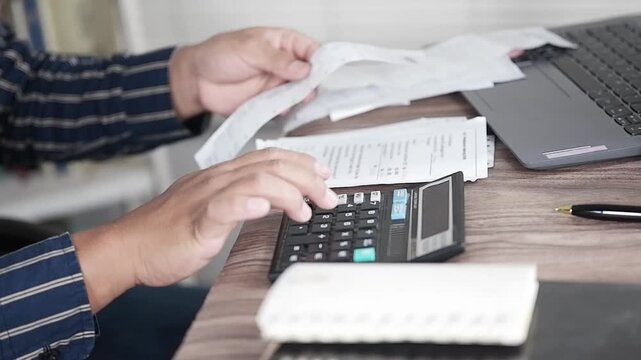 Close-up of a man's hands looking at a shopping receipt and calculating it with a calculator. Invoices, calculating household budgets, household expenses. Insurance or mortgages. Household financial m