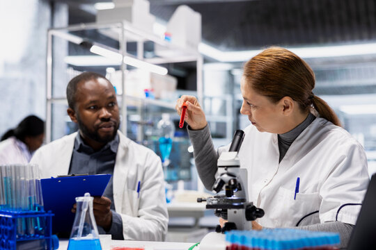 Female researcher and lab colleague testing blood samples for adverse drug reactions. Team of scientists brainstorming, evaluating sanguine fluid vials to ensure medication safety standards, camera A