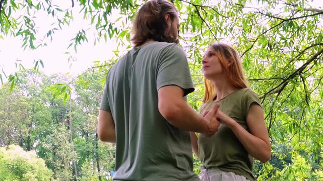 tender embrace of young loving couple outdoors in lush green summer forest man with long hair beard holding woman with reddish hair as she leans head on his chest both smiling gently eyes closed