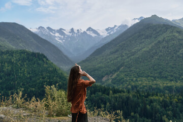 Naklejka premium A woman stands on a hillside gazing at snow capped mountains in a lush valley, capturing a tranquil outdoor landscape and wide open nature