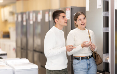 Young couple chooses modern fridge at a hypermarket