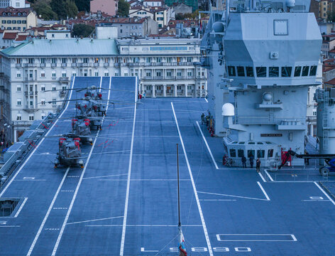Aerial view of helicopters lined on the deck of the LHD Trieste, its flight control tower prominent against the cityscape, Trieste, Italy.