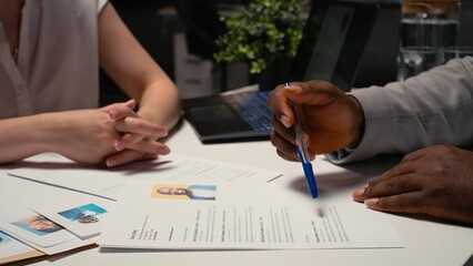 Close up of CV document evaluation in a corporate job interview, businesswoman asking african american candidate questions based on his past work experience and studies shown on paper. Camera A.