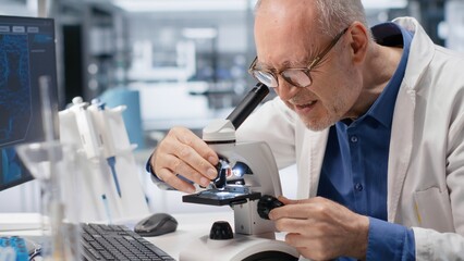 Professional science expert uses microscope as observation tool with glass tray of samples. Experiment combines molecular biology, genetics research and analysis to drive medical discovery.