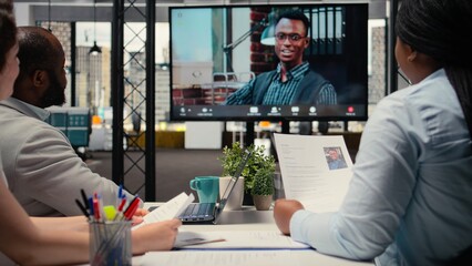 Recruiters team and male candidate engage in a video call discussion with webcam and high tech tools, reviewing the resume and job search progress during a remote interview conference. Camera A.