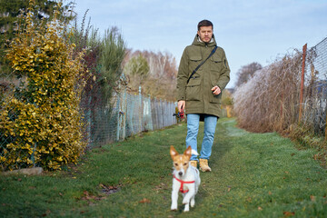 Man walking small dog on leash along green pathway outdoors