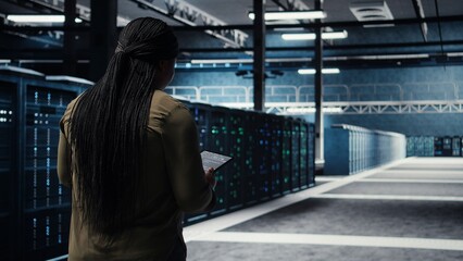High tech data center technician uses tablet to develop disaster recovery plans, minimizing downtime. IT employee walking in server room, enhancing data protection protocols using device, camera A