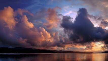 Golden sunlight illuminates picturesque puffy clouds reflected in the calm waters of a tranquil lake at dusk creating a peaceful and serene natural landscape.