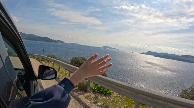 Woman enjoys freedom during road trip by car. Hand extending outside car window, feeling smooth breeze while cruising scenic coastal highway, embracing sense of freedom and joyful travel