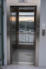 Modern glass elevator with stainless steel doors and city traffic visible through windows. Urban architecture and public infrastructure in Athens, Greece.