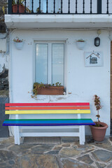 Banco pintado con la bandera arco iris en la entrada de una vivienda.