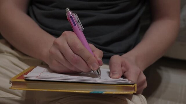 Casual journaling in dim room, Focus on fingers and pen strokes, meditative close-up writing, Engaged in mindful writing with soft cushions around in subdued environment