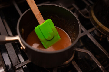 a green spatula in a black pot with heated sugar on a stove top making homemade caramel