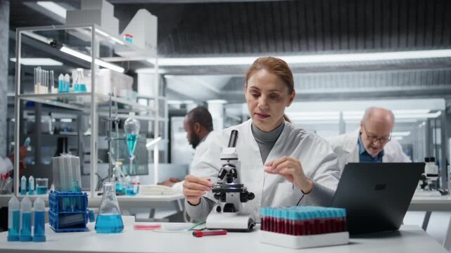 Histology technician in lab inspecting thin glass slide for structural defects or impurities. Woman in laboratory conducting visual quality control check using compound microscope, camera A