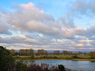 Cloudy sky over a river with trees and fields in the background