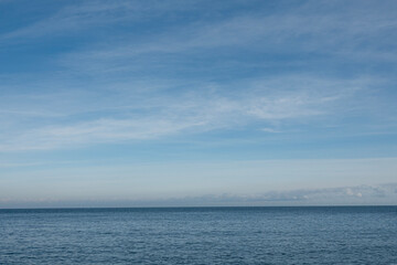Obraz premium Ocean water meets the horizon under a blue sky with clouds
