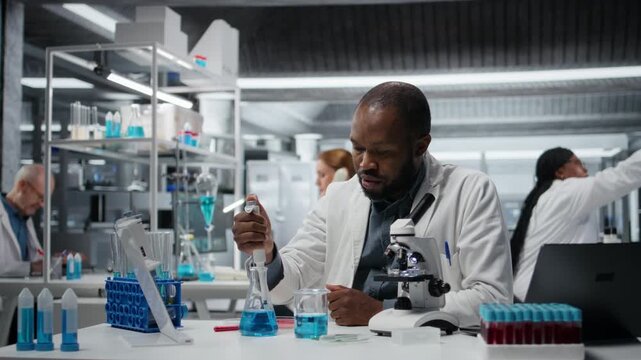 Analytical chemist pipetting blue liquid into test tube to analyze it. African american man transferring chemical sample in glass flask to prepare for spectroscopic analysis, camera A