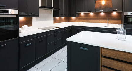 Modern kitchen interior presenting black shaker cabinets, white quartz countertops, island, and...