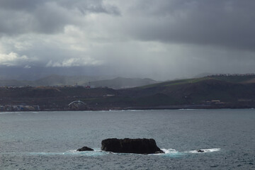Gran Canaria, view towards the main body of the island from El Confital beach on the edge of Las Palmas de Gran Canaria, rain sweeping through the island

