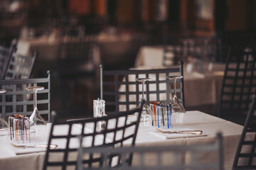 Tables are set in a restaurant with glasses and utensils neatly arranged. The setting shows an inviting atmosphere for dining. The scene captures the preparation before guests arrive