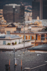View of rooftops in a city with various antennas standing tall. Buildings form the backdrop with clear skies. The scene captures urban life and infrastructure in the daylight hours