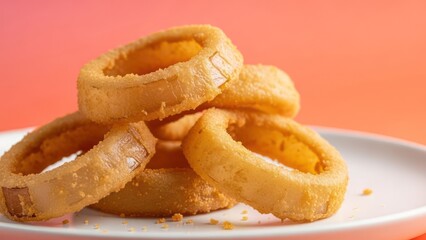Close up of golden onion rings on a white plate against a warm gradient background
