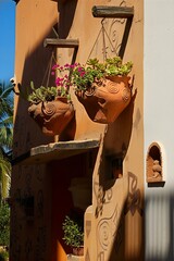 Decorative wall features hanging clay pots with vibrant plants, adorned with traditional patterns and a charming bird sculpture under warm sunlight.