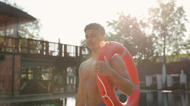 Young man working as a shirtless lifeguard at a swimming pool, ready to ensure safety and protection on a sunny day. Male holding lifebuoy