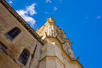 Upward view of an ornate Gothic church tower adorned with sculpted gargoyles and intricate stone carvings, set against a vivid blue sky in Nevers. The image highlights historic architecture, textured