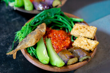 Indonesian spicy (sambal) on an earthenware plate with fried eggplant, fried tempeh, fried salted...