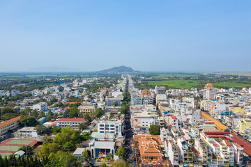 Obraz premium Wide aerial panorama of Chau Doc, Vietnam, showing a central avenue lined with colorful buildings, green fields stretching into the distance, and a prominent mountain rising on the horizon under a
