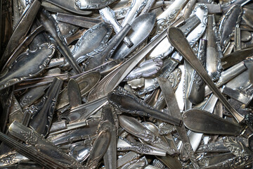 Close-up view of a pile of vintage silverware and flatware, featuring ornate handles and worn...