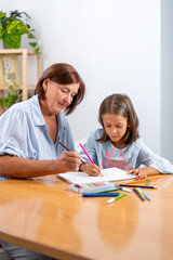 Grandmother helping granddaughter with drawing using colored pencils at home, showing education, creativity and family bonding between generations