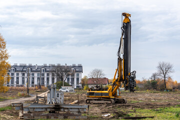 A large yellow and black construction machine is in the foreground. A building is in the...