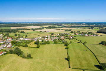 Drone view of Saint-Germain-Chassenay with a charming village surrounded by lush green meadows, hedgerows, and expansive farmland beneath a clear blue sky. The landscape is open, sunlit, and peaceful