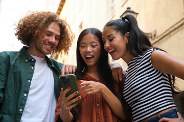 Three young tourists are looking at a smartphone and laughing, enjoying their vacation in a european city