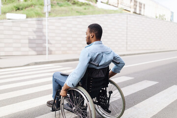 Young black man in wheelchair using crosswalk outdoors, copy space. Millennial African American man...