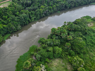 Aerial View of Small Boat Navigating River Through Dense Tropical Forest