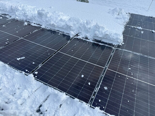 CLOSE UP: Black solar panels with a thick blanket of snow covering part of the array. Winter clearing and maintenance of a home solar power plant and enabling energy production during the cold season.