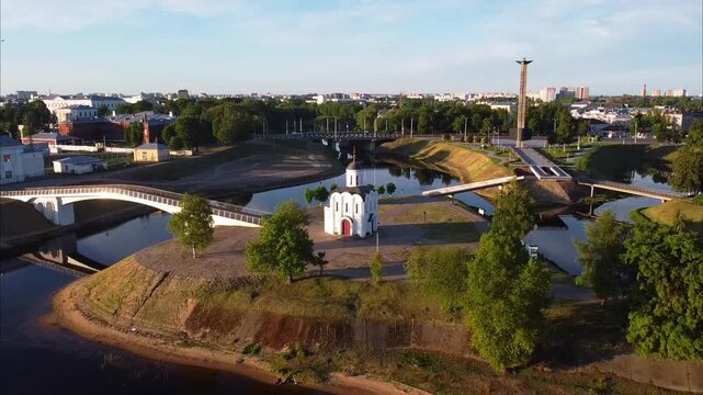A drone flies backward over Tver, first showing a church on an island and the Victory Obelisk, then revealing city buildings, the Volga River, and the waterfront.